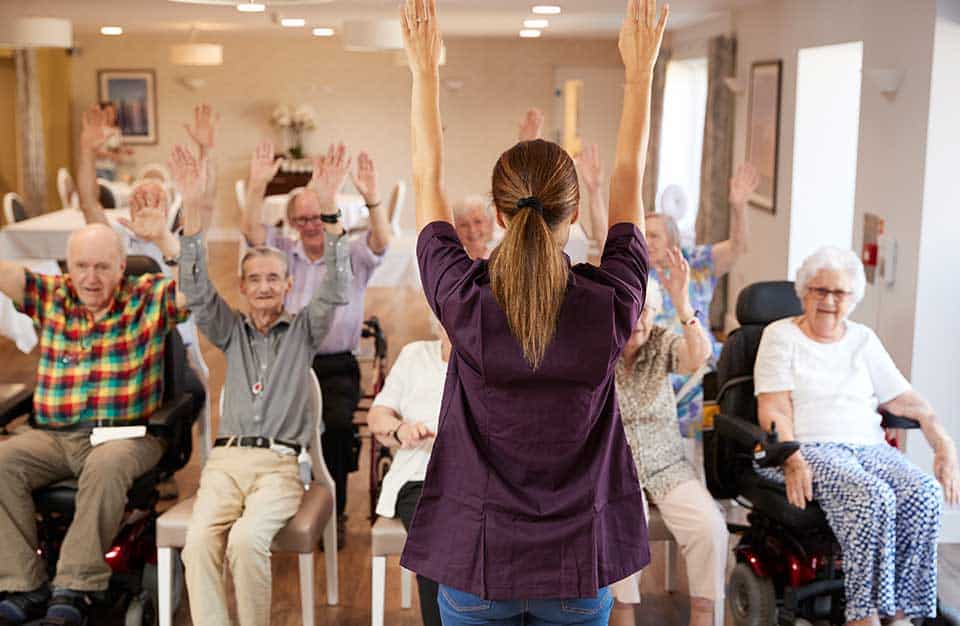 a group of elderly people sitting in chairs with their hands up